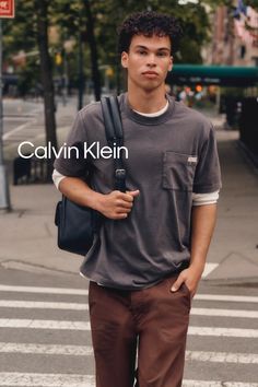 Young man with curly hair wearing a t-shirt and brown pants on a city street