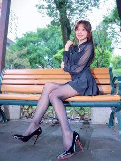 Woman in a black dress and pantyhose sitting on a park bench