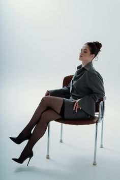 Woman in a pinstripe suit and black stockings sitting on a chair