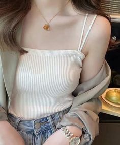 Woman in a white ribbed tank top and denim jeans with a gold necklace