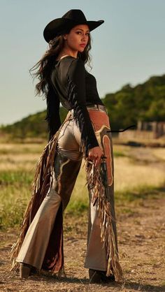 Woman in a cowboy hat and chaps holding a gun outdoors