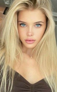 Woman with long blonde hair and blue eyes wearing a brown top and necklace