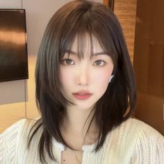 Woman with dark layered hair and bangs wearing a white cardigan indoors