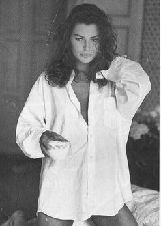 Woman in an unbuttoned white shirt holding a cup in a bedroom