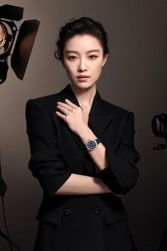 Woman in a black blazer and watch posing in a studio with soft lighting