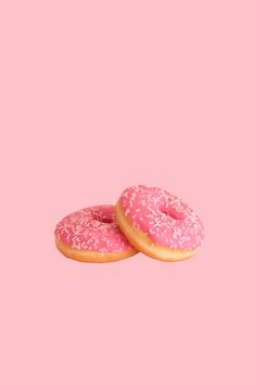 Two pink frosted donuts with sprinkles on a solid pink background