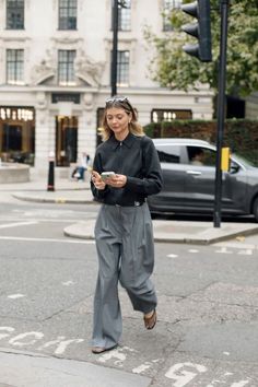 Woman in a dark gray jacket and wide leg pants walking on a city street