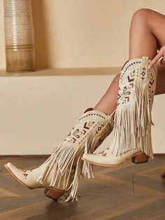 Close up of a person wearing cream cowboy boots with fringe and embroidery