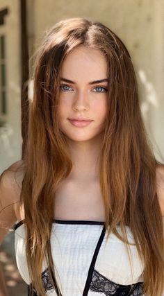 Woman with long brown hair and blue eyes wearing a white top with lace trim