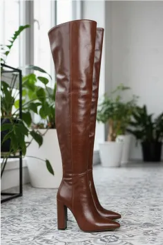 Pair of brown thigh-high boots with high heels on a tiled floor indoors