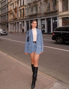 Woman in a denim jacket and skirt with knee-high boots on a city street