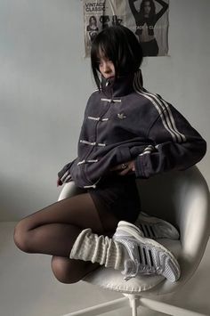 Person with short black hair wearing an Adidas jacket, tights, and leg warmers, sitting indoors