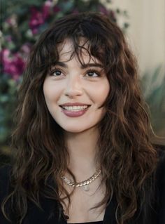 Woman with long wavy hair and bangs smiling outdoors