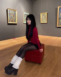 Woman with long black hair sitting on a red ottoman in an art gallery