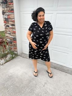 Woman in a black floral dress and flip flops standing outdoors