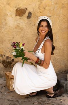 Woman in a white dress and crochet headscarf holding flowers outdoors