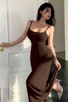 Woman in a brown dress and high heels posing by a white door