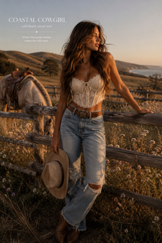Woman in a lace top and ripped jeans holding a cowboy hat at golden hour