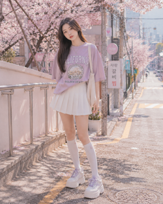 Woman in a purple t-shirt and white pleated skirt on a cherry blossom lined street