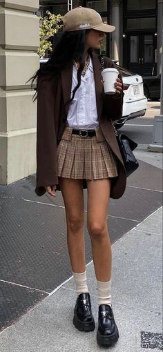 Person in a plaid skirt, brown blazer, and baseball cap on a street