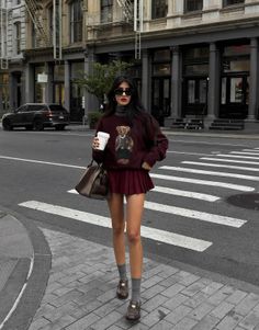 Woman in a sweater and pleated skirt holding a coffee cup on a city street