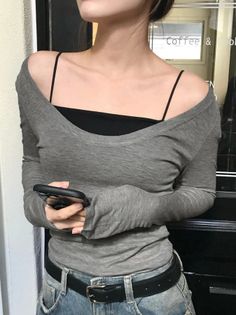 Woman in an off-shoulder top and jeans holding a phone indoors