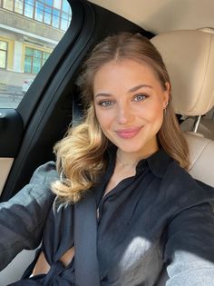 Woman with long hair and a black shirt smiling in a car