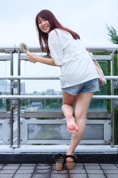 Woman in denim shorts and a white t-shirt smiling on an outdoor bridge