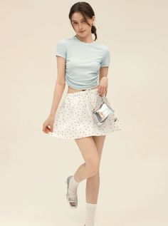 Woman in a light blue crop top and polka dot skirt holding a silver bag