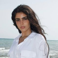 Woman with long dark hair wearing a white shirt at the beach
