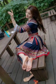 Woman in a traditional dress sitting on a wooden bench with bare feet