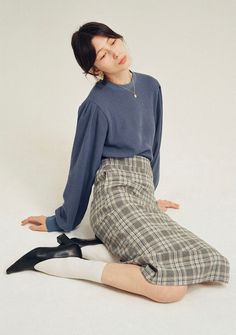 Woman in a blue sweater and plaid skirt sitting on a white floor