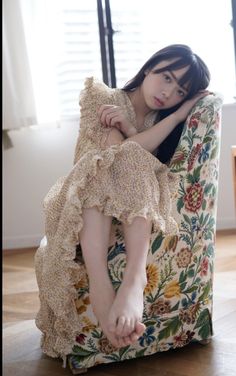 Woman with long dark hair in a floral dress sitting on an armchair indoors