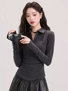 Woman in a dark gray long-sleeve shirt and black skirt holding a camcorder