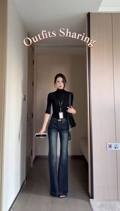 Woman in a black turtleneck and flared jeans holding a phone and handbag