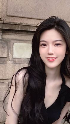 Woman with long black hair smiling in a black top outdoors