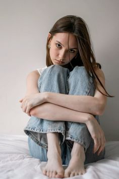 Young woman with long hair sitting on a bed in blue jeans, looking at the camera