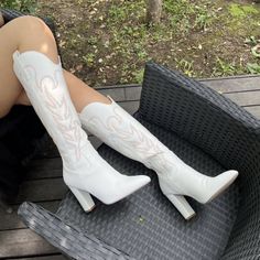 Person wearing white cowboy boots with embroidery, sitting outdoors