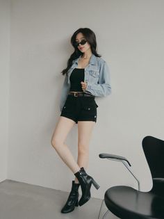 Woman in a denim jacket, black shorts, and sunglasses posing indoors