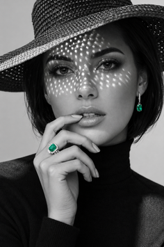 Woman in a straw hat and black turtleneck with emerald jewelry