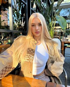 Woman with long blonde hair wearing a crop top and bomber jacket at an outdoor cafe