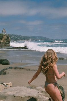 Woman in a bikini on a beach with ocean waves and a gazebo on a cliff