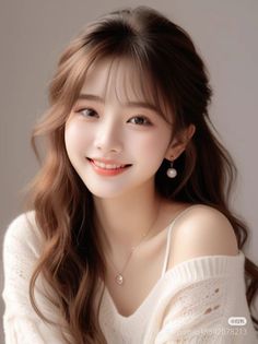 Smiling woman with long wavy hair wearing an off-shoulder sweater and pearl earrings