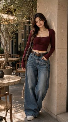 Woman in a maroon crop top and baggy jeans leaning against a wall at an outdoor cafe