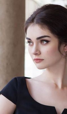 Woman with dark hair in a black dress looking to the side