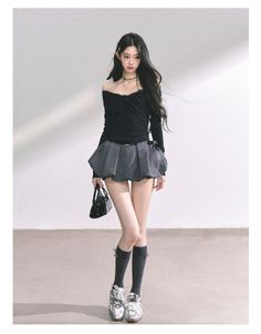 Woman with long dark hair wearing an off-shoulder top and mini skirt in a studio