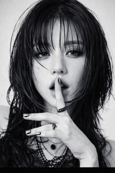 Woman with wet black hair and dark makeup, finger on lips, in black and white