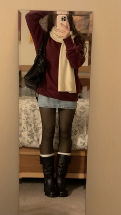 Person in a maroon sweater, denim skirt, and black boots taking a mirror selfie