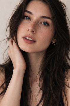 Woman with long dark hair, blue eyes, and freckles in a soft-lit portrait