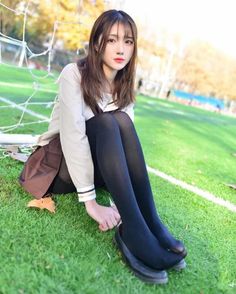 Young woman in a school uniform and black tights sitting on green grass
